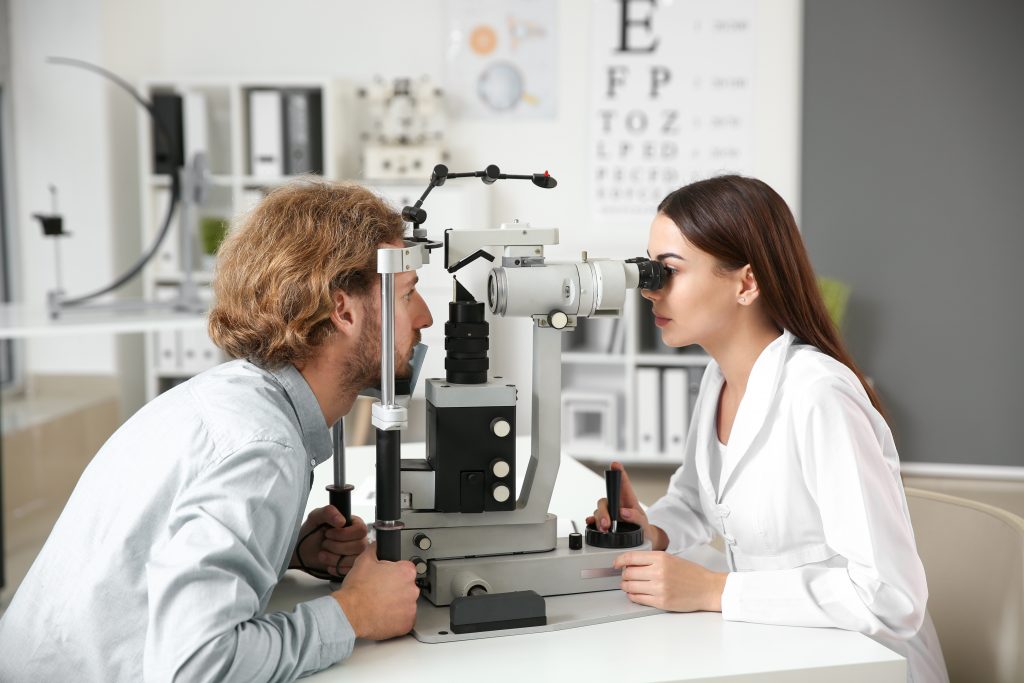 Homem e mulher em um exame oftalmológico, com o homem olhando para um aparelho e a mulher ajustando o equipamento.