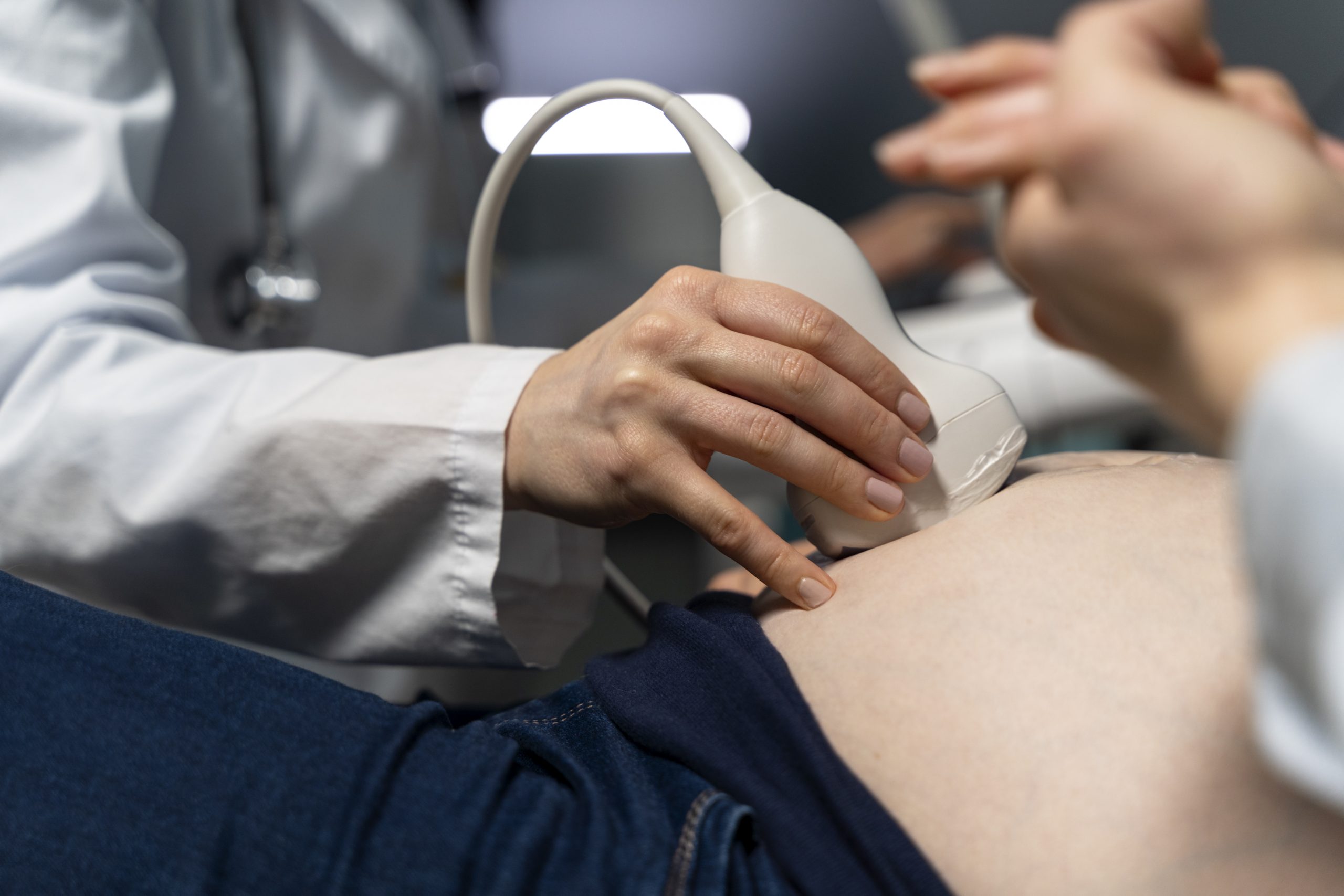Médica realizando ultrassom em uma gestante deitada, com foco na barriga.