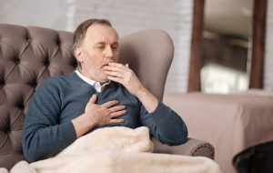 Terrible bronchitis. Senior handsome man is coughing really strongly while sitting on couch at home and.