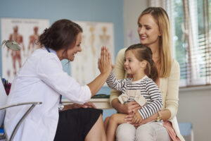 doctor giving high five smiling girl sitting her mother 039 s lap medical appointment Central de Consultas | Clínica Popular