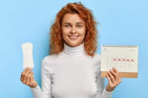 female hygiene concept redhead smiling woman holds clean period sanitary napkin pad menstruation calendar Central de Consultas | Clínica Popular