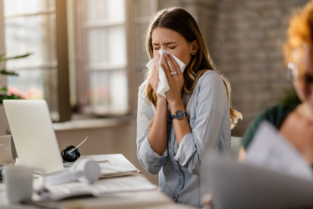 young sick businesswoman sneezing tissue while working office Central de Consultas | Clínica Popular