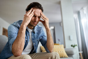 low angle view distraught man holding his head pain while sitting living room Central de Consultas | Clínica Popular